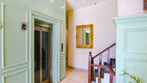 Un pasillo con una puerta verde, una escalera de madera y un espejo en la pared.