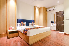 Una habitación de hotel moderna con una cama grande, un armario de madera y una mesita de noche con artículos de aseo.
