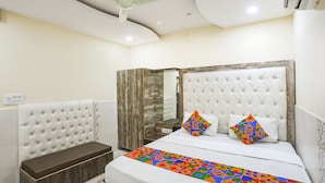 A bedroom with a tufted headboard, a bed with colorful bedding, a bench, and a ceiling fan. - Fabhotel Welcome (Kanpur)