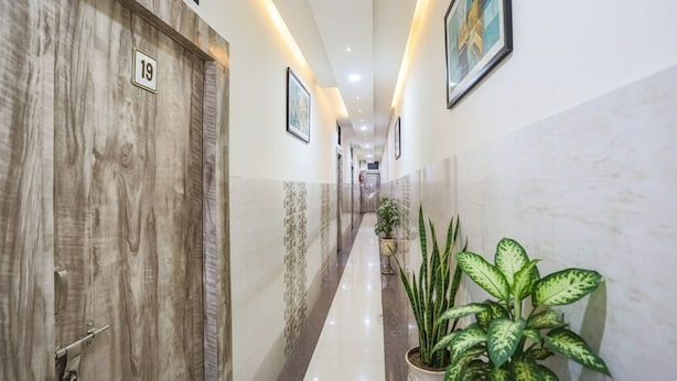 A hotel hallway with wooden doors, numbered room signs, framed artwork, and potted plants. - Fabhotel Welcome (Kanpur)