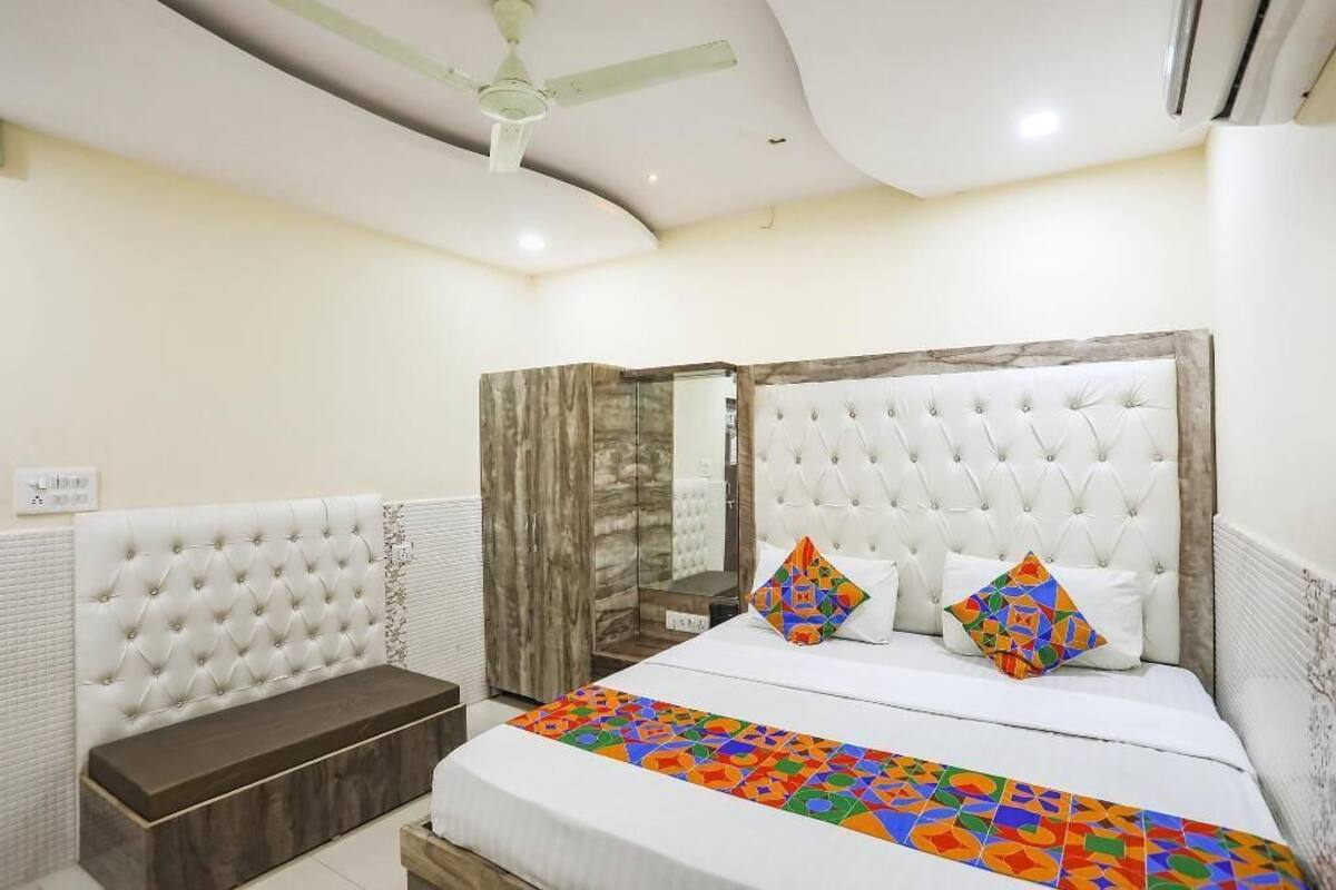 Un dormitorio con cabecera capitonada, un banco, una cama con ropa de cama colorida y un ventilador de techo.