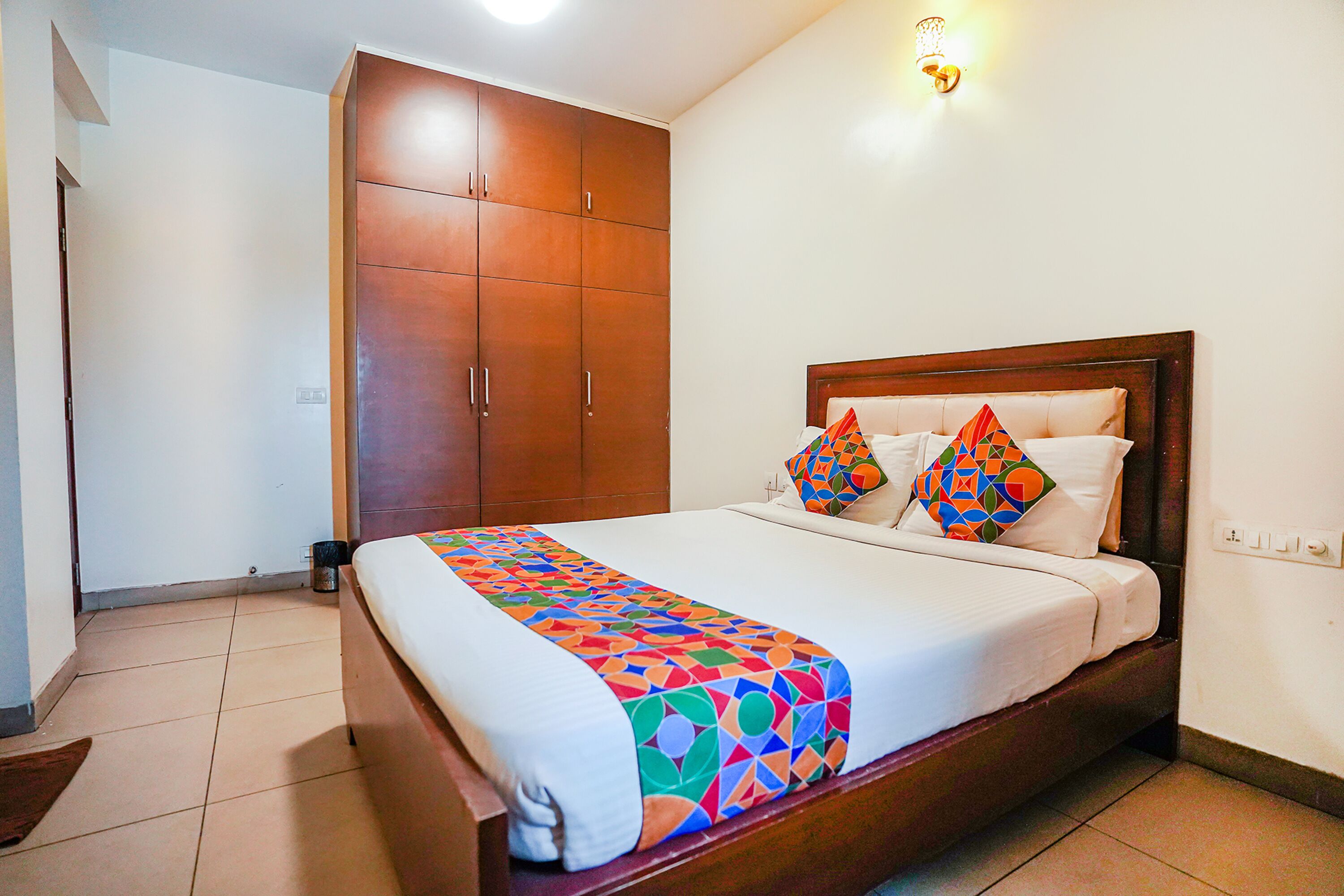 A hotel room with a large bed, a wardrobe, and a wall-mounted light fixture.
