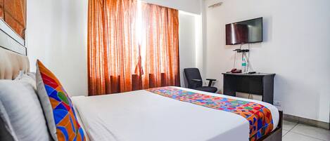 A hotel room with a bed, a desk, a chair, a TV, and an air conditioning unit.