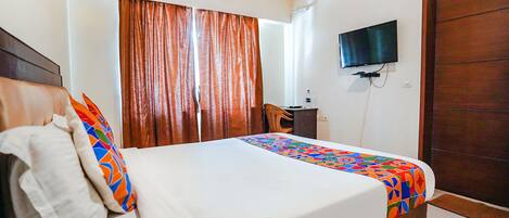 A neatly made bed with a colorful bedspread, a television mounted on the wall, and a wooden door.