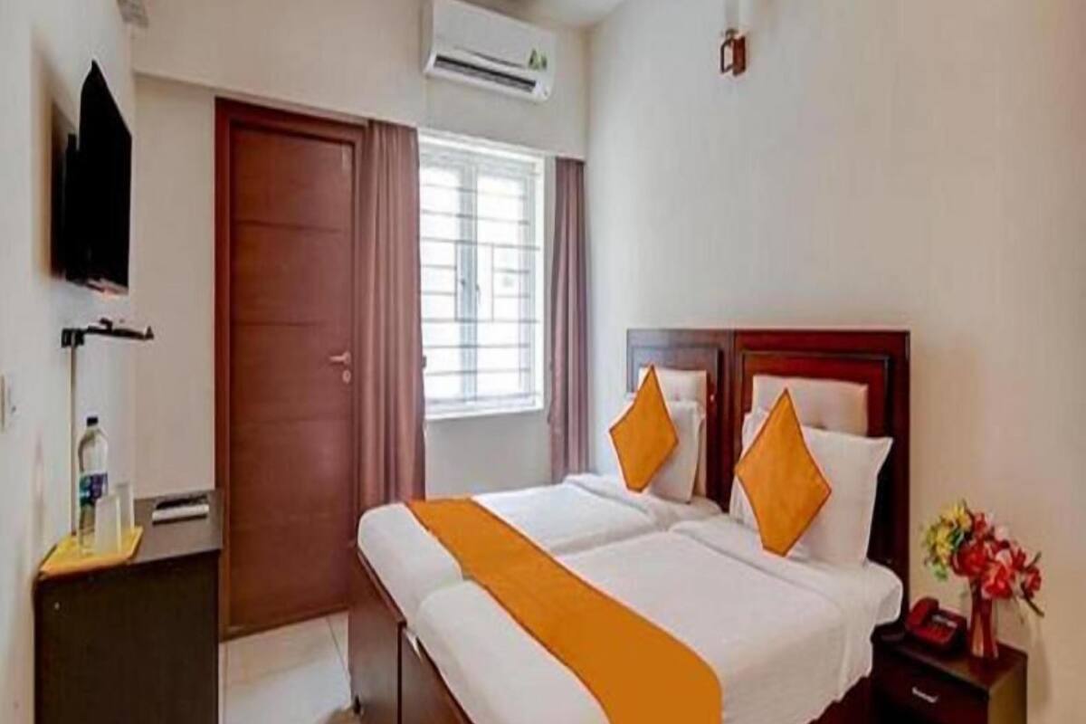A hotel room with a bed, a nightstand, a desk, an air conditioning unit, and a window with curtains.