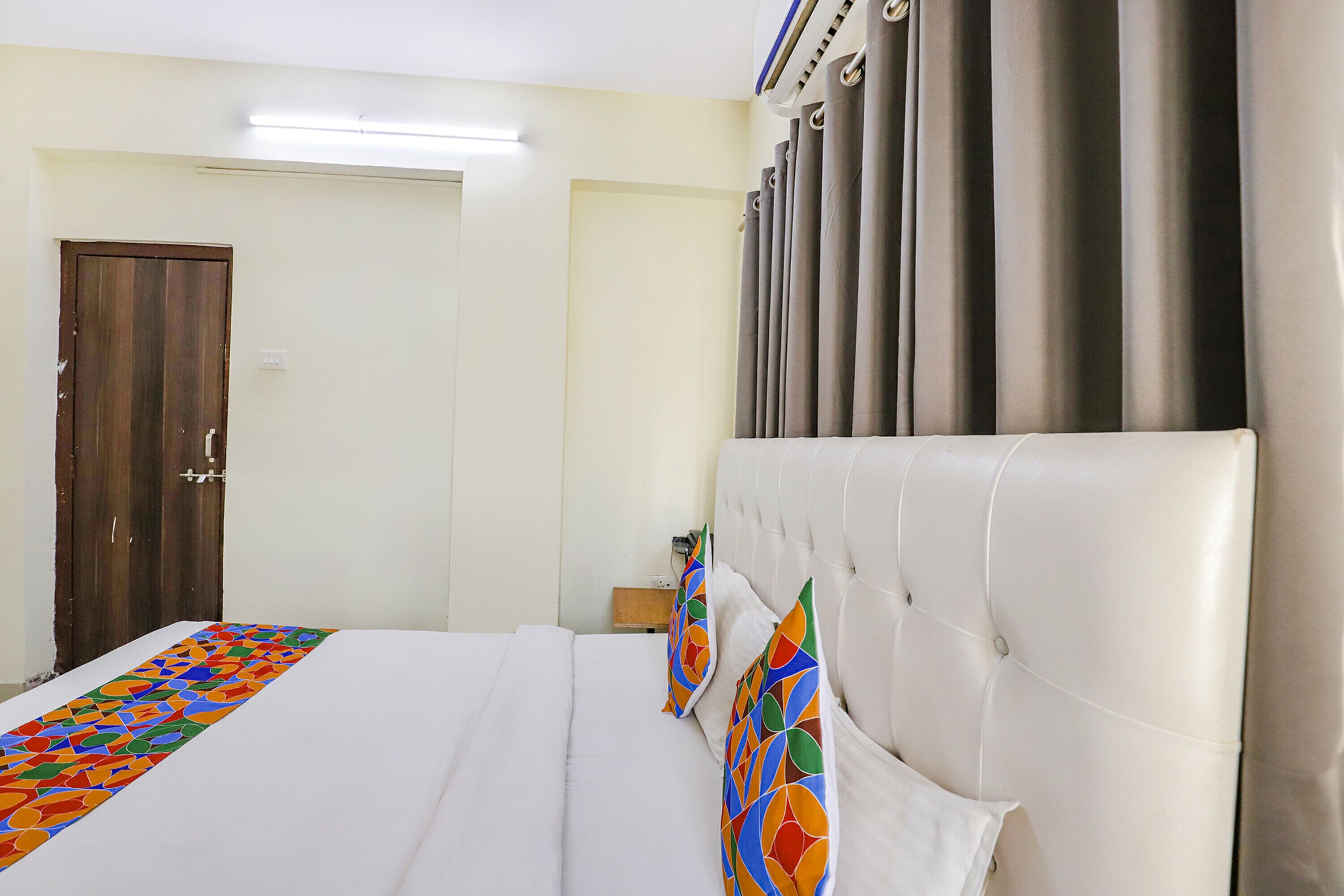 A hotel room with a large bed, a wooden door, and a window with curtains.
