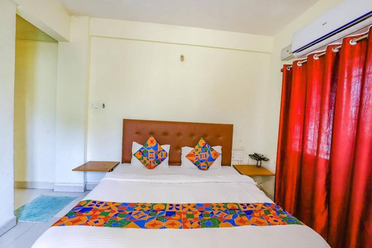 Un dormitorio con cama, cabecera, mesita de noche, cortina roja y ventana.