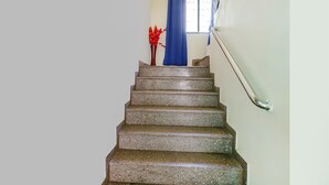 Una scala con corrimano, una finestra con tenda blu e un vaso con fiori rossi.