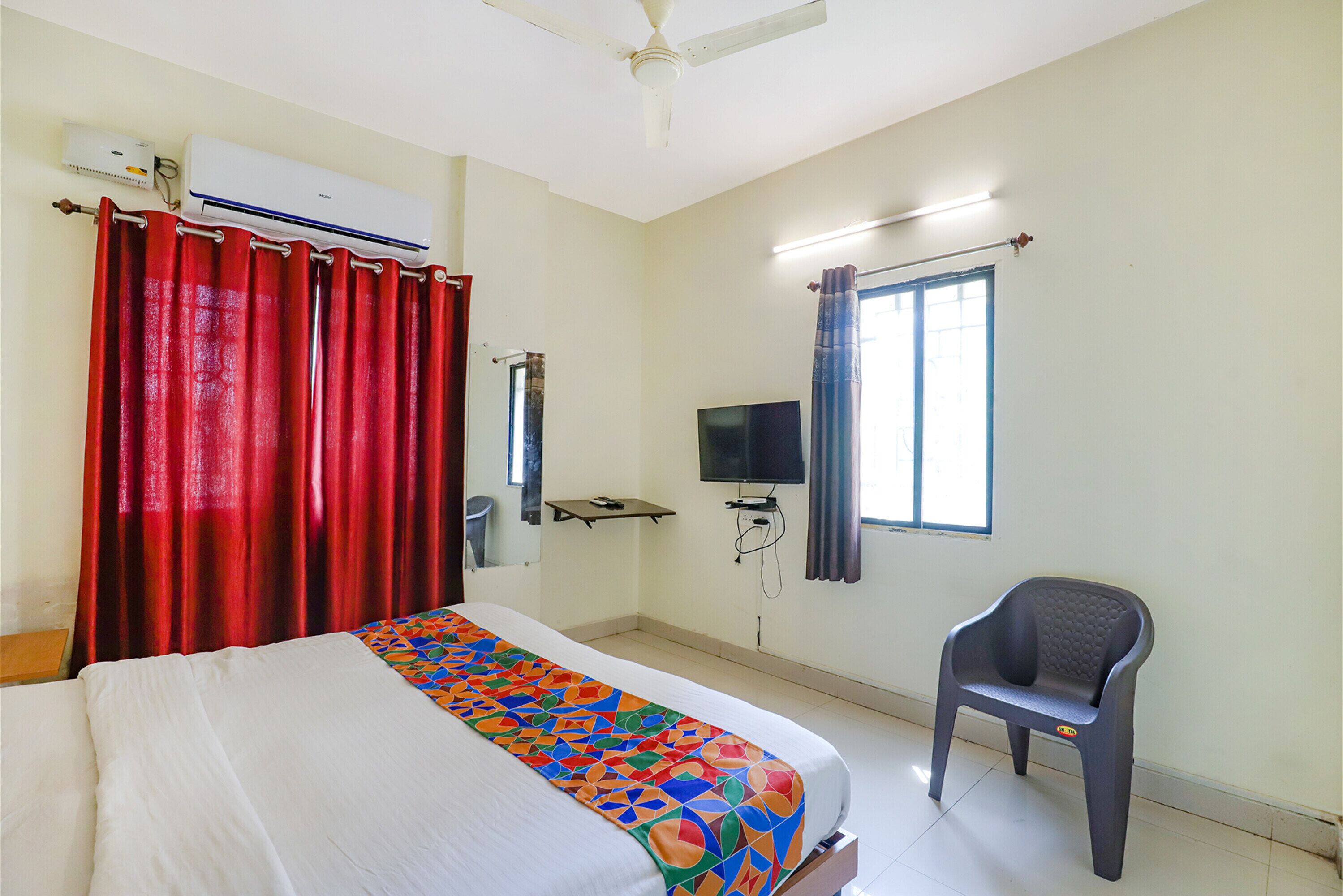 A hotel room with a bed, a TV, a chair, and an air conditioning unit.