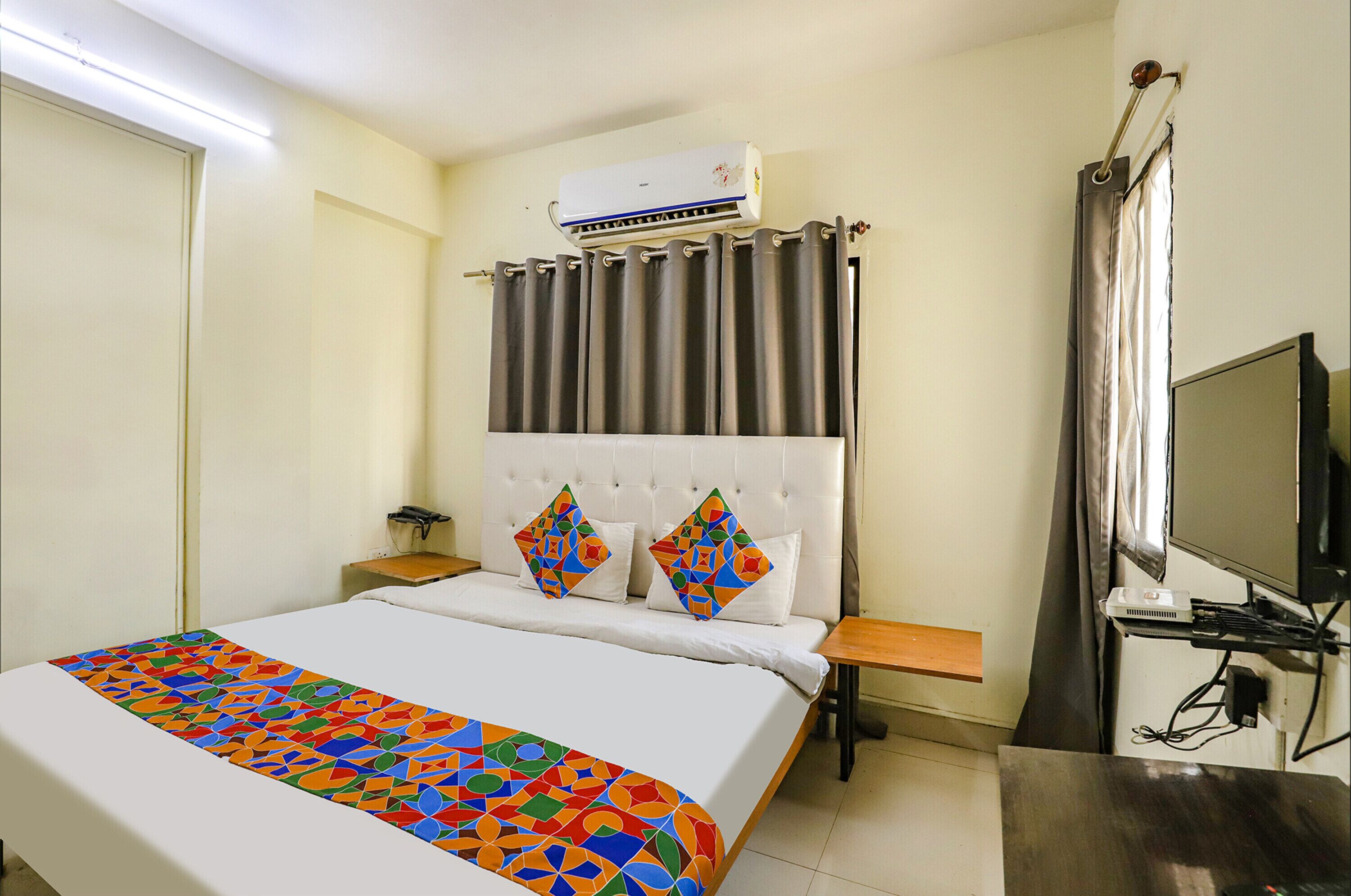 Una habitación de hotel con cama, televisión, aire acondicionado y cortina.
