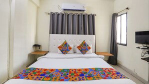Una camera d'albergo con un letto, una televisione, un condizionatore d'aria, una finestra con tende e un telefono sul comodino.