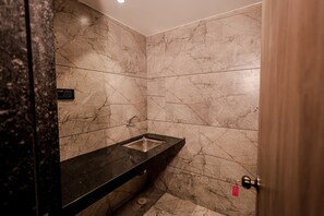 Une salle de bain aux murs de marbre, avec un lavabo noir et une porte dotée d’une serrure rouge.