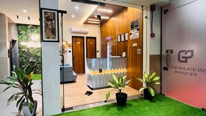 Zona de recepción de hotel con diseño moderno, que incluye un mostrador de recepción, un área de espera con asientos y césped artificial verde en el exterior.