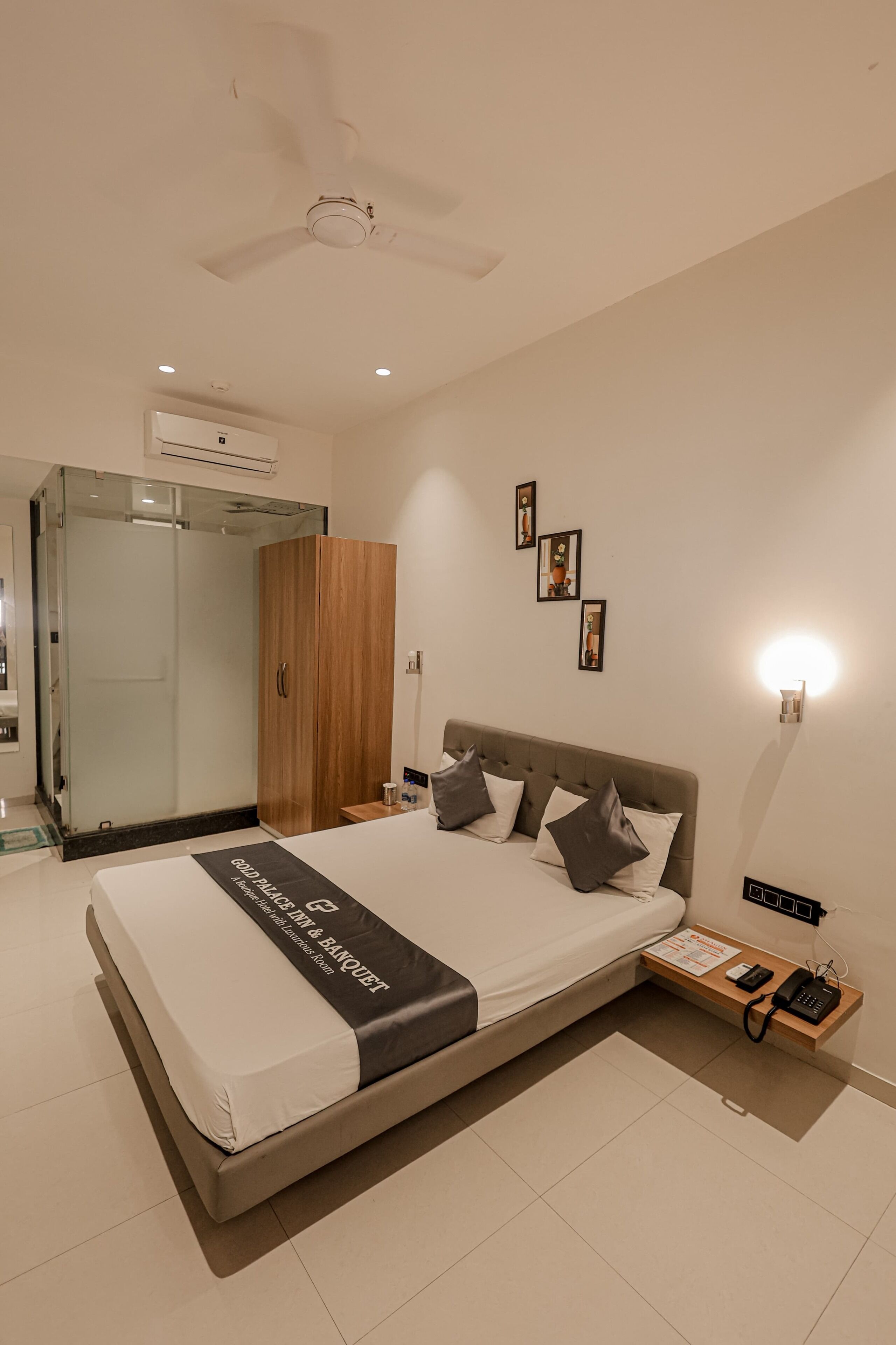 Une chambre d’hôtel moderne dotée d’un grand lit, d’une armoire en bois, d’une douche en verre et d’un ventilateur de plafond.