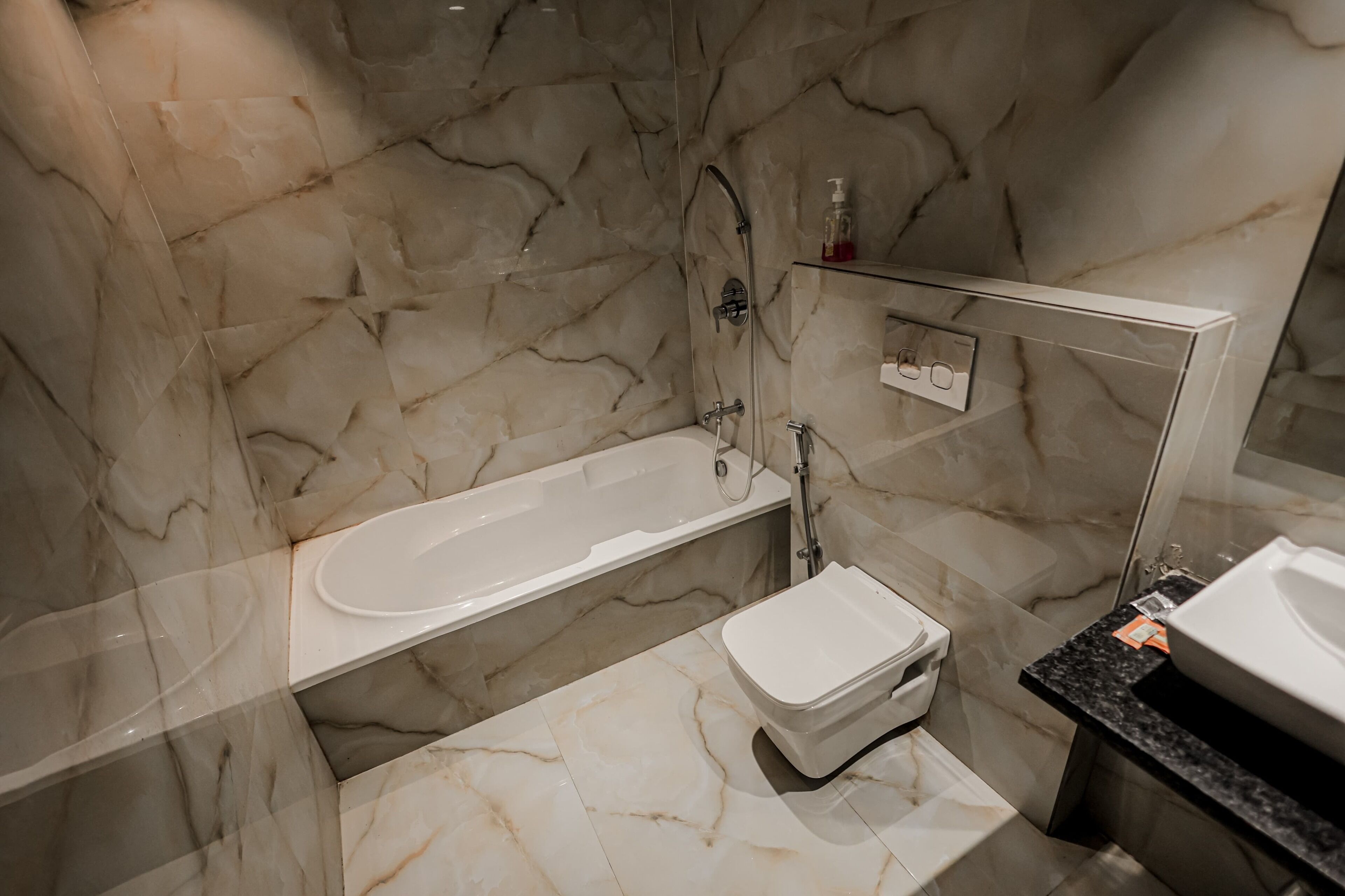 Un baño con pared de mármol, una bañera, un inodoro y un lavabo.
