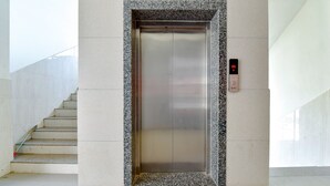 Un ascensor con pantalla digital, un borde de mármol y una escalera a la izquierda.
