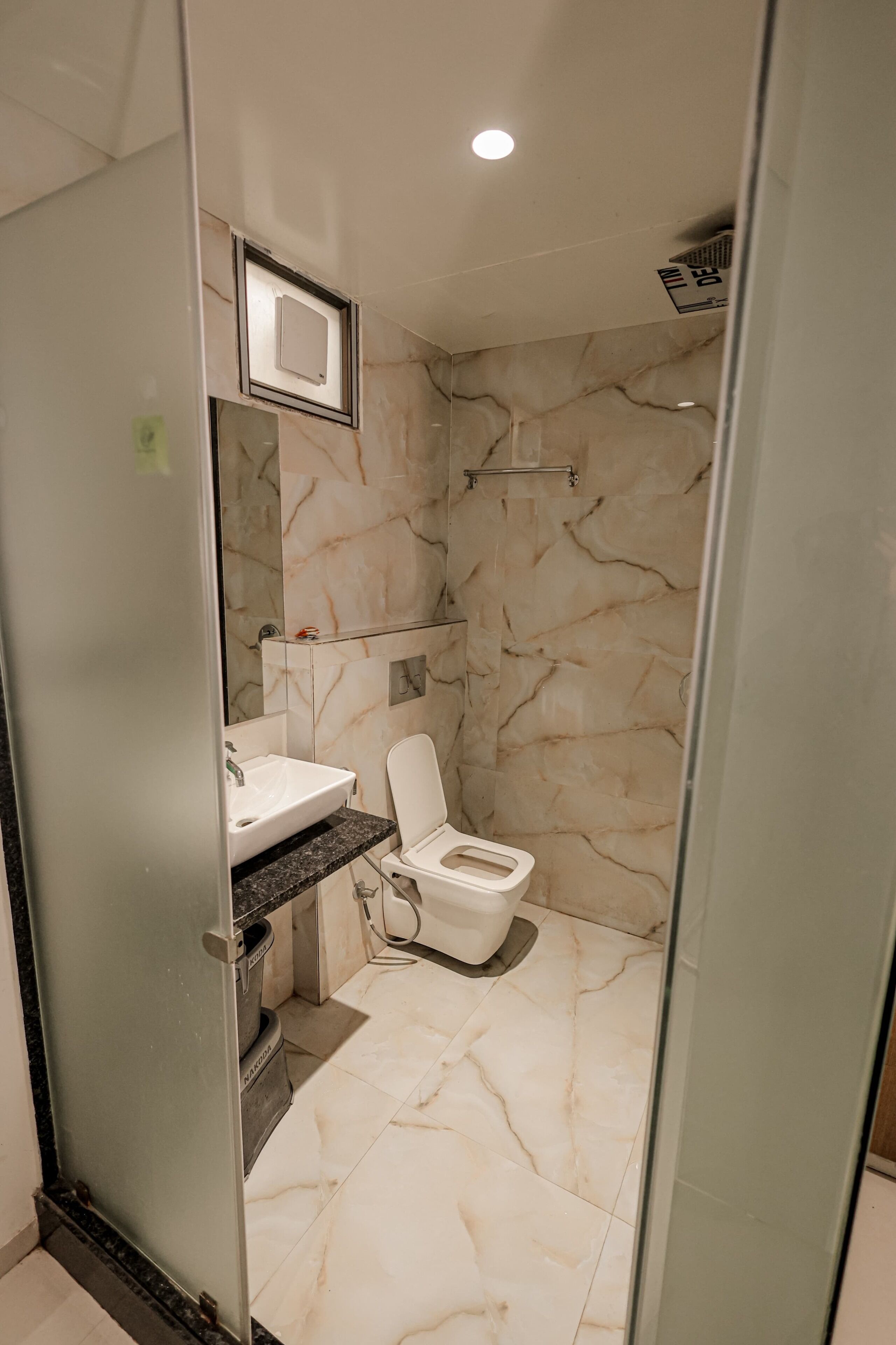 Un bagno moderno con pavimento in marmo, un WC bianco, box doccia in vetro e un piccolo lavandino con piano in marmo.