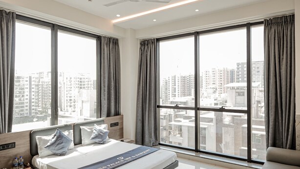 Una habitación de hotel moderna con una cama grande, un ventilador de techo y vistas de la ciudad a través de amplias ventanas.