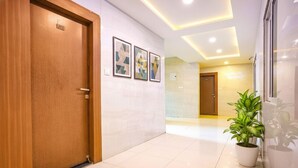Un pasillo con una puerta de madera con la etiqueta “212”, una planta en maceta y tres cuadros en la pared.