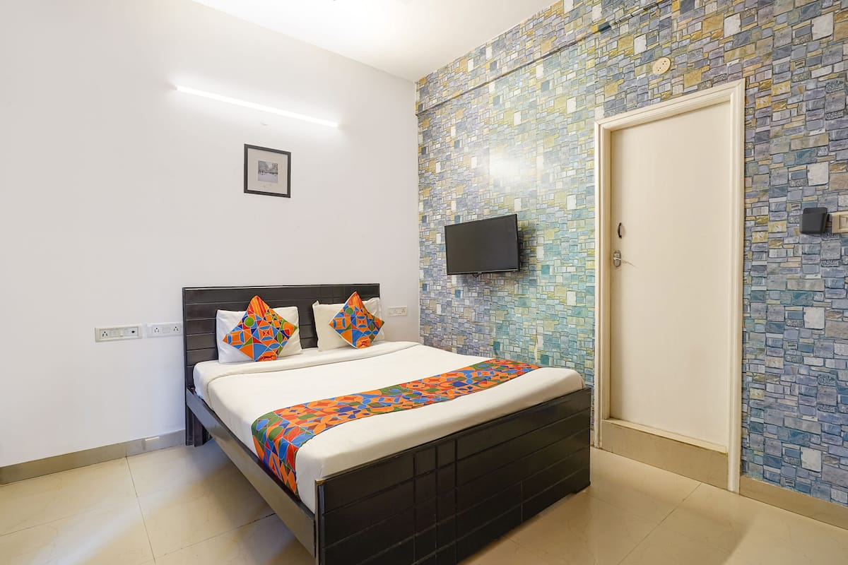 A neatly made bed with a patterned bedspread, a flat-screen TV mounted on the wall, and a tiled mosaic wall.