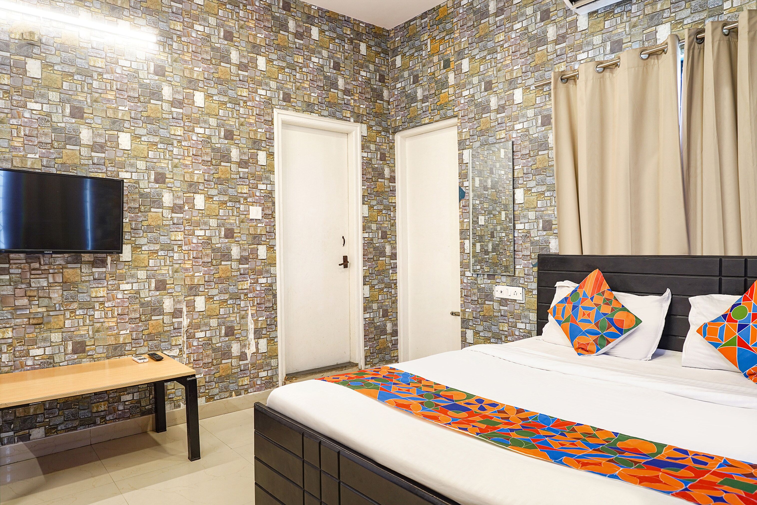 Un dormitorio con pared de mosaicos, una cama con almohadas coloridas, una mesita de noche y un televisor de pantalla plana.