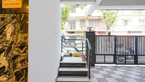 A staircase leading to an upper floor with a checkered floor pattern, a metal railing, and a sign warning about the coronavirus. - FabHotel Kings Suites Banaswadi (Bengaluru)