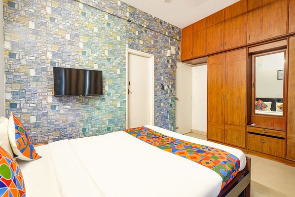 A bedroom with a bed, a television mounted on the wall, and wooden wardrobes.