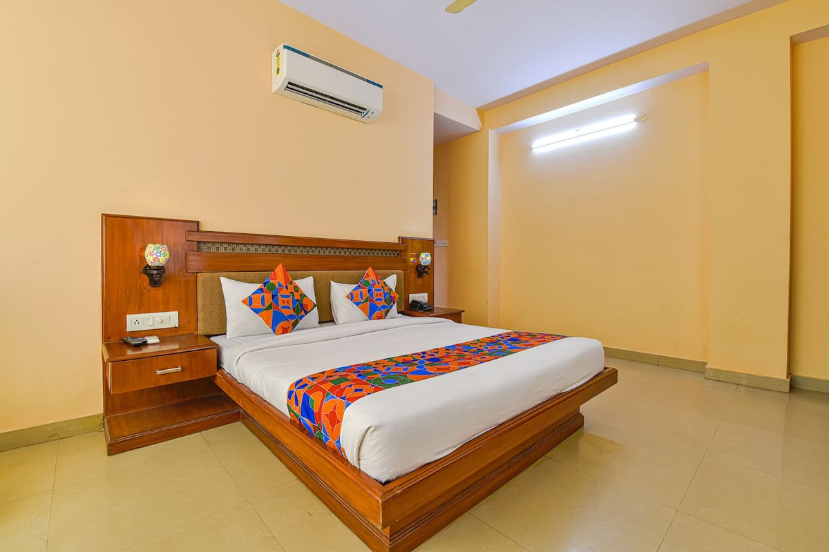Habitación de hotel con cama de madera, mesita de noche, aire acondicionado y lámpara fijada a la pared.