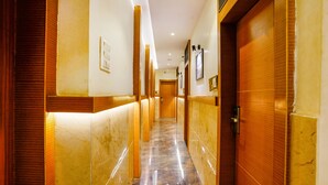 Un pasillo de hotel con suelo de mármol, paneles de madera y una puerta de madera al final.