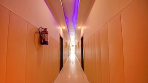 Un pasillo largo y estrecho con extintor en la pared, puertas a ambos lados y techo con iluminación empotrada.