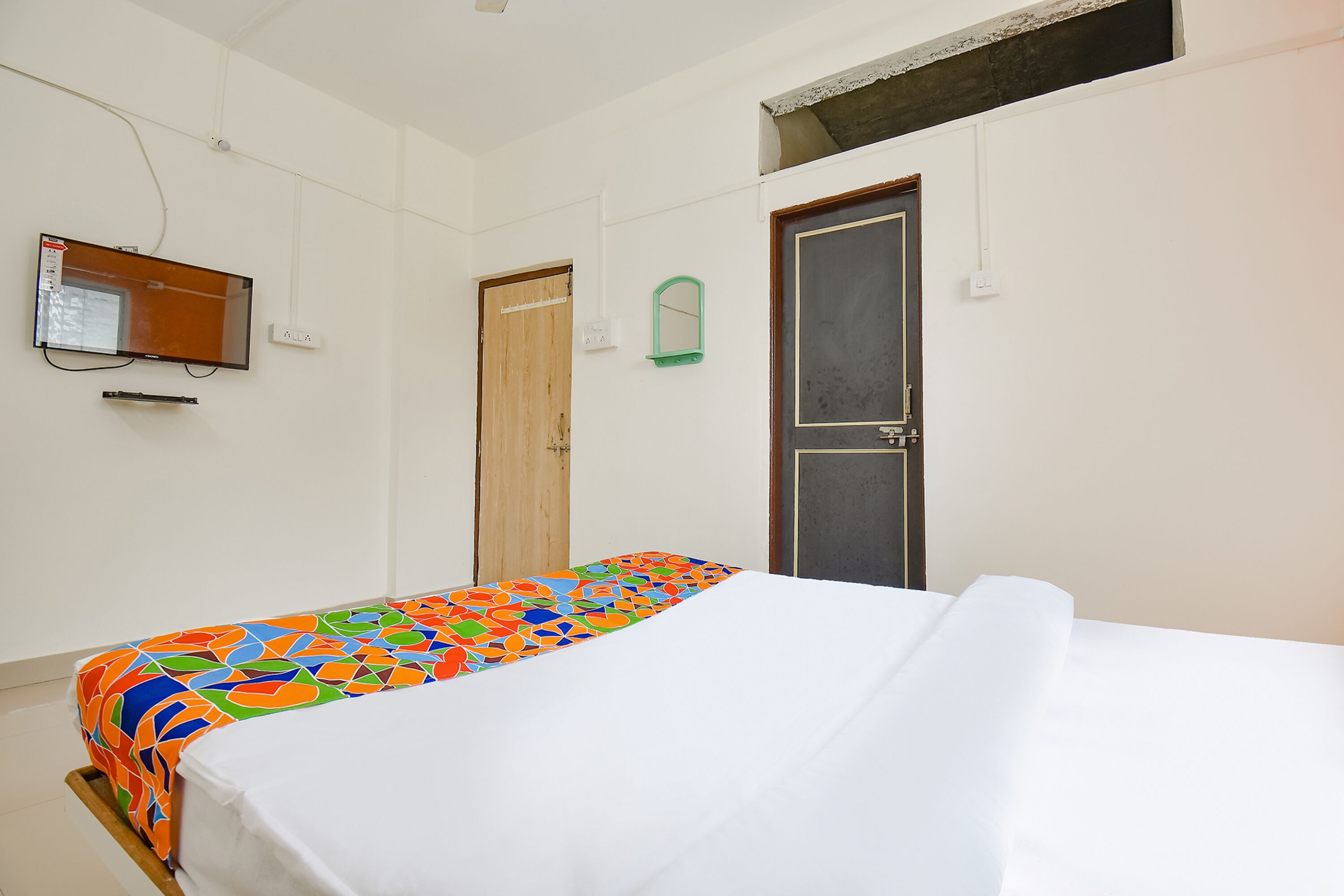 A room with a bed, a television mounted on the wall, and a door.