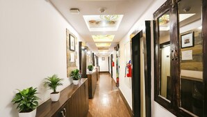 A hotel hallway with a wooden floor, potted plants, framed pictures, and a fire extinguisher. - FabHotel Veetara (New Delhi)