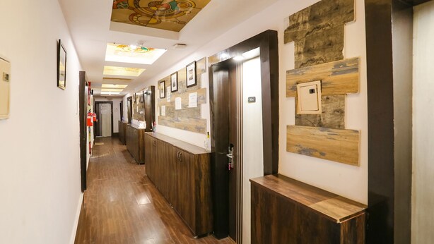 A hotel corridor with wooden flooring, a ceiling with a decorative design, and walls adorned with framed pictures and a wooden panel. - FabHotel Veetara (New Delhi)