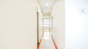 Un pasillo largo y estrecho con paredes blancas y piso brillante, que conduce a una habitación luminosa con ventana.