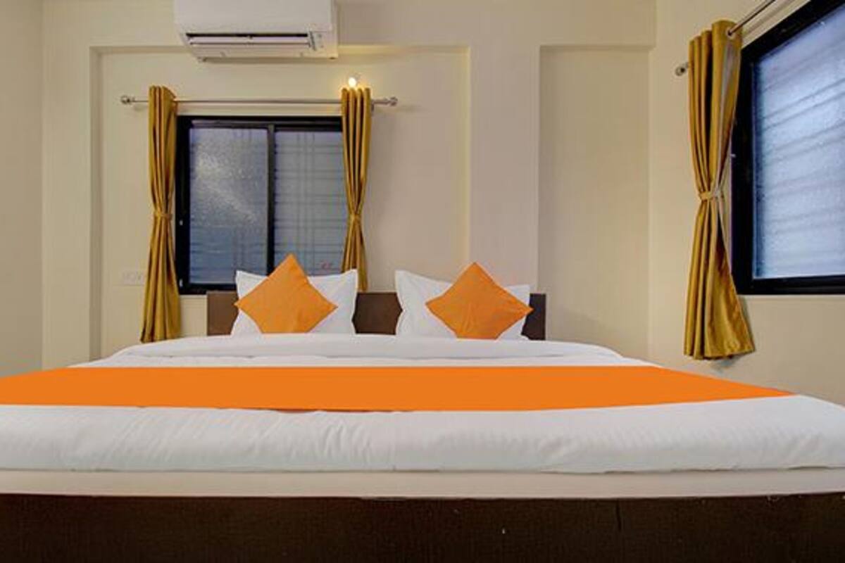 A hotel room with a bed, curtains, an air conditioning unit, and a window.