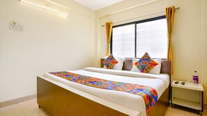 Una habitación de hotel con una cama grande, una mesita de noche, una ventana con cortinas y una lámpara fijada a la pared.