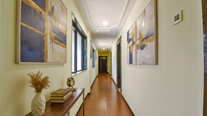 A hallway with artwork on the walls, a wooden bench with a vase and books, and a door at the end.