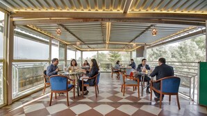 A covered outdoor dining area with tables and chairs, large windows, and a checkered floor.