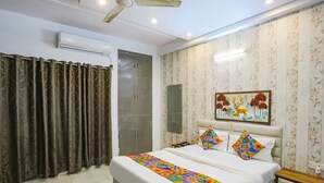 Un dormitorio con cama, cortinas, ventilador de techo, unidad de aire acondicionado, armario, mesita de noche y una obra de arte colgada en la pared.