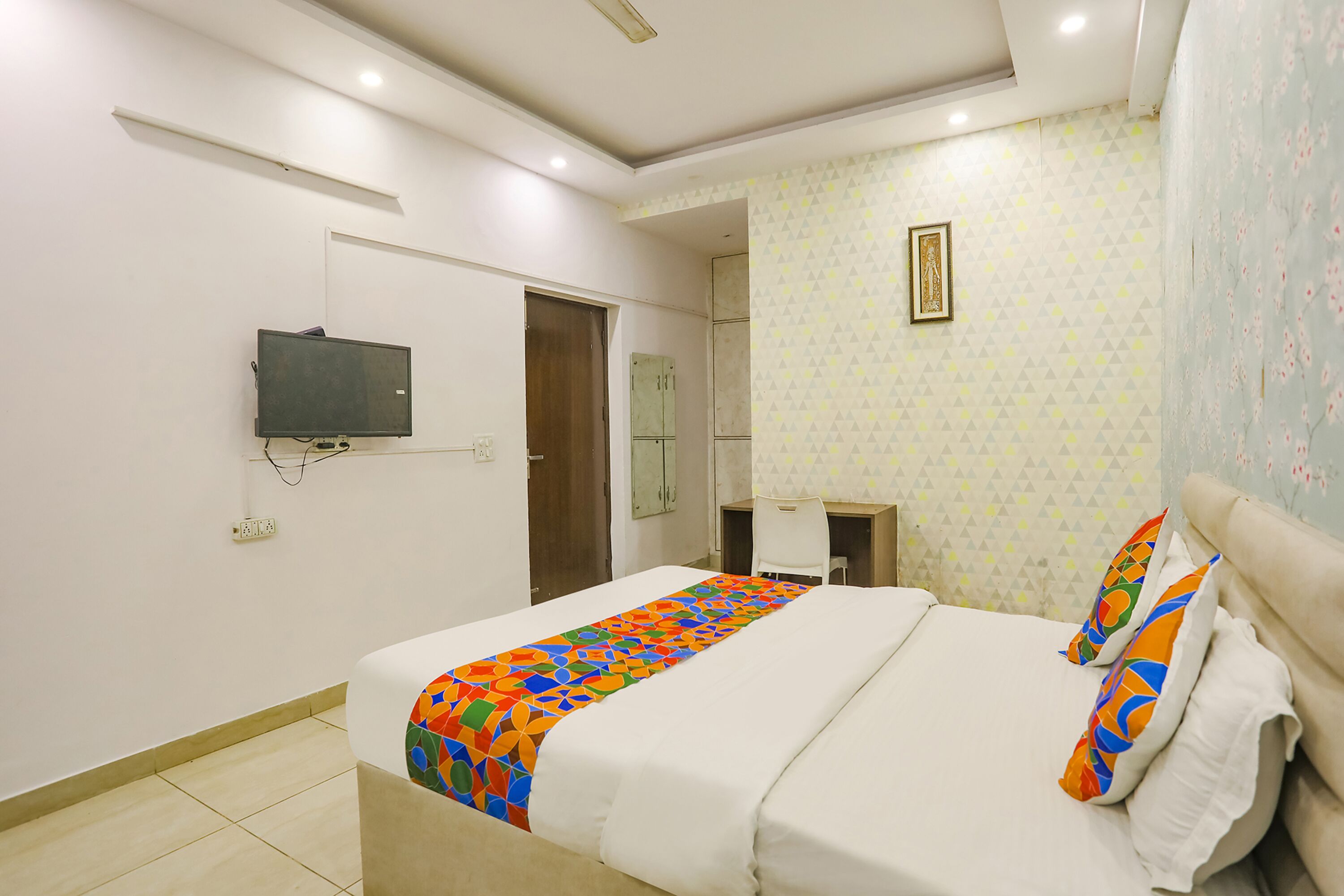 A hotel room with a bed, a desk, a chair, a TV, and a door.