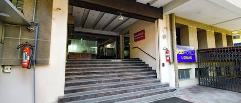 Entrada de un hotel con una escalera que conduce al vestíbulo, un extintor de incendios en la pared y un cartel que indica 'Lotus Grand Restaurant'.