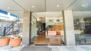 Entrada de un edificio moderno con puerta de vidrio, una escalera a la izquierda y plantas en macetas afuera.