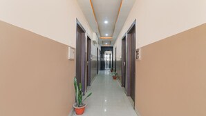 A long, narrow hallway with doors on both sides, potted plants, and a ceiling with orange lighting accents. - Fabhotel Vinayaka (Patna)