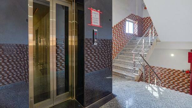A hotel lobby with a glass elevator, a staircase with patterned tiles, and a fire alarm on the wall. - Fabhotel Vinayaka (Patna)