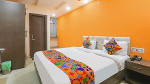A hotel room with a bed, a nightstand, a wardrobe, and an orange wall. - Fabhotel Vinayaka (Patna)