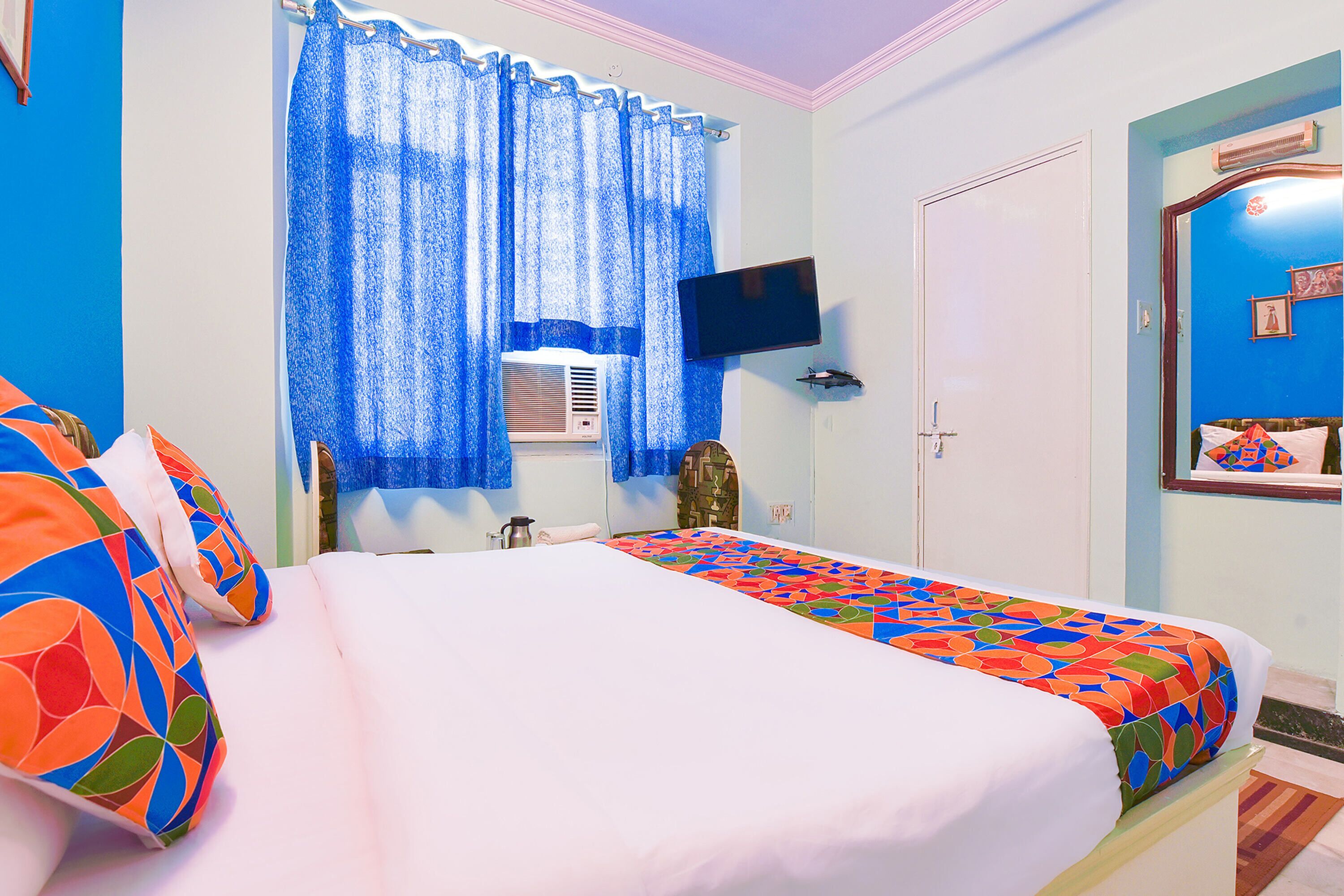 A hotel room with a bed, a television, a window with curtains, and a door.