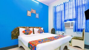 Quarto com cama, mesa pequena, cadeira e janela com cortinas.