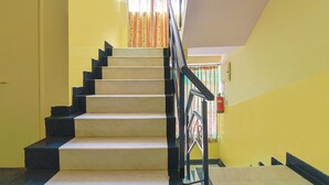 Uma escadaria com degraus alternados em preto e branco, um corrimão de metal e uma parede amarela.