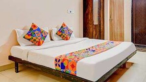 A neatly made bed with a colorful bedspread and pillows, a wooden wardrobe, and a door in a well-lit room. - FabHotel Blusky (New Delhi)