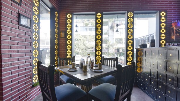 A restaurant with a brick wall, a large window with decorative yellow patterns, and a black metal counter. - FabHotel Prime AV Royale (Dehradun)